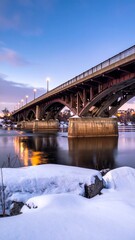 A photograph showcases an old, arched bridge at dawn over a river. Snow blankets the foreground. Lights glow along the bridge