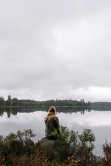 Person sitting by calm forest lake under overcast sky © Nordic Stock Studio