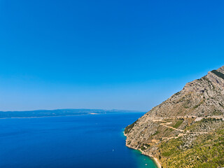 Fototapeta premium A picturesque view of a mountain serpentine road by a bright blue sea under a clear sky