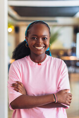 Smiling woman stands with arms crossed in a modern caf&eacute; during the daytime in a lively atmosphere