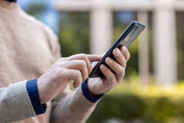 Close-up photo of a body part, hands of a young man in a sweater and shirt standing on the street,...