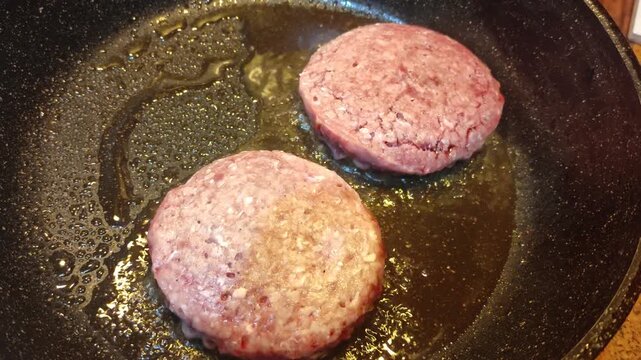 Two raw beef patties sizzling in a frying pan, close-up shot, home cooking