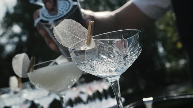 Pouring cocktail through strainer into crystal coupe glass