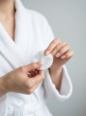 Naklejka premium Woman in white bathrobe holding a cotton pad for skincare routine