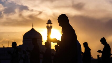 Fototapeta premium Silhouette of Muslim men praying at sunset in front of a mosque