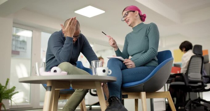 Two professionals discuss ideas in a modern office space with casual seating and an engaging atmosphere while focusing on teamwork and problem-solving tasks