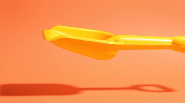 Bright Yellow Toy Shovel on Orange Background with Hard Shadow.