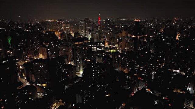 Night aerial view pushing in toward city with Altino Arantes building in Sao Paulo, Brazil. Drone shot revealing red Farol Santander landmark and terminal