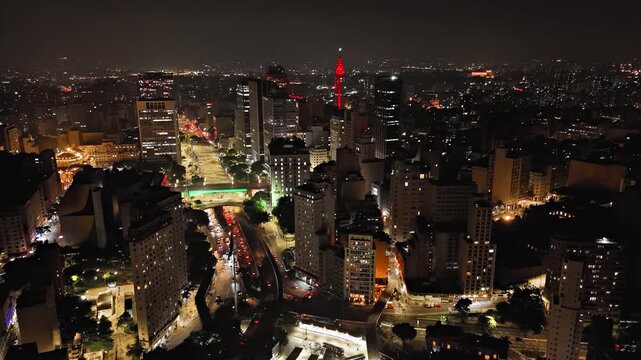 Static night aerial view of avenue intersection with Viaduto do Cha and Altino Arantes building in Sao Paulo, Brazil. Fixed drone shot revealing green illuminated viaduct and Farol Santander