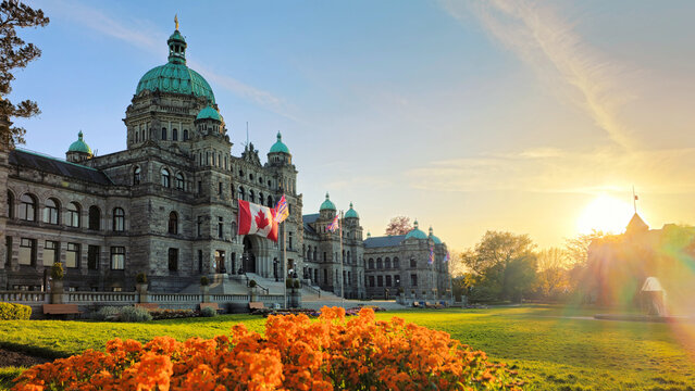 Historic British Columbia provincial parliament building with vibrant flowers and setting sun, Victoria, BC, Canada
