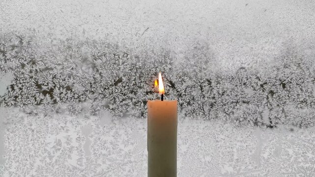 A candle burns against the background of a frozen window №1