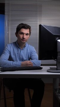 Vertical video man looking directly at viewer while sitting at a desk with a monitor and keyboard, representing concepts of office work, technology use, and professional tasks