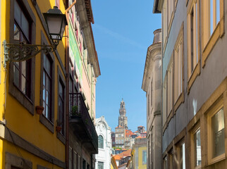 Fototapeta premium Narrow colorful street with historic tower view in Guimaraes Portugal. Traditional European buildings framing urban skyline under clear blue sky. Travel destination, architectural heritage,