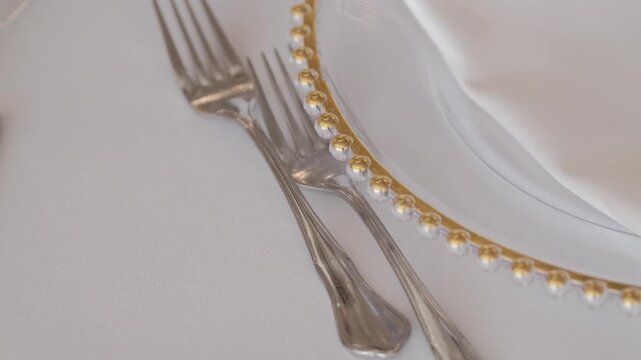 Extreme close up of elegant silverware and a glass charger plate with gold beaded rim on a white tablecloth