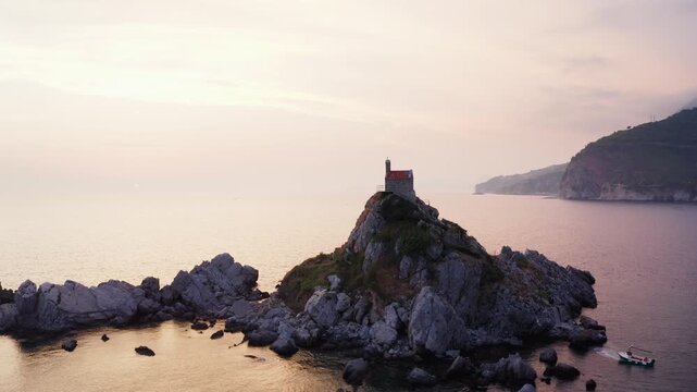 Flying drone 4K video around Sveta Nedjelja Island with magestic small church on cliff's top during evening sunset time hours. Balkans traveling, landmarks and Nature concept in Petrovac, Montenegro.