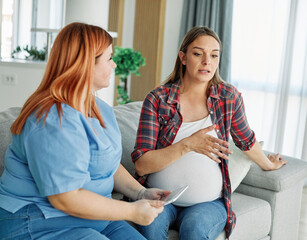 Portrait of a young happy pregnant woman doing exam with doctor or nurse during a visit at home or...