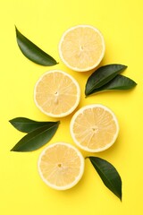 Fototapeta premium Pieces of ripe lemons and leaves on yellow background, flat lay