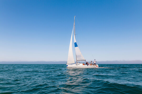 Sailboat Sailing on Open Ocean With Crew Enjoying Sunny Day and Calm Blue Waters