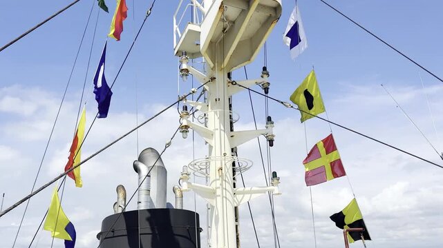 Close-up of ship's mast and black exhaust funnel with decorative signal flags strung along the rigging, representing seafaring traditions, international communication, and holiday spirit.