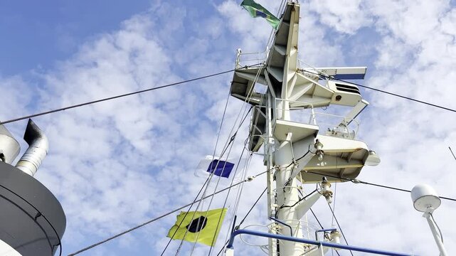 Nautical holiday celebration featuring a towering white radar mast adorned with vibrant geometric signal flags flapping in the ocean breeze on a sunny day aboard a massive cargo vessel.