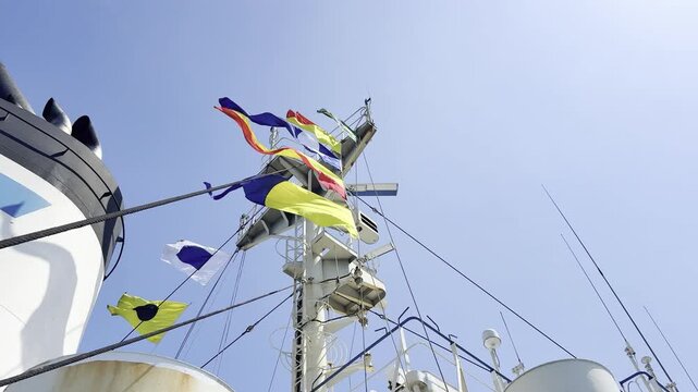 Low angle view of a cargo vessel's white mast fully decorated with bright international code flags, celebrating a maritime festival or national holiday with the crew on the ocean.