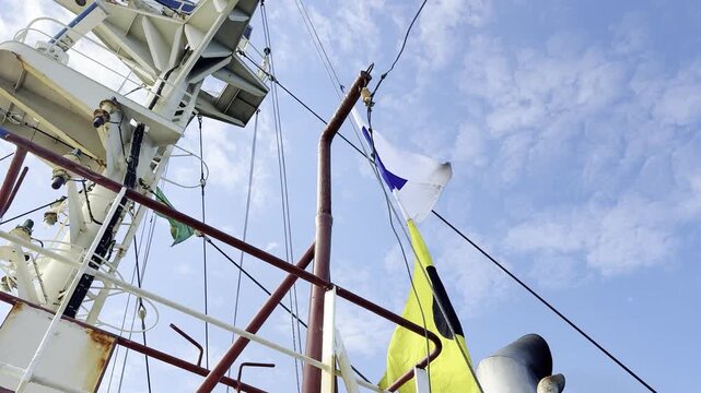 Colorful maritime signal flags fluttering on a ship's mast against a blue sky, illustrating the naval tradition of dressing ship for holidays, festive ceremonies, and celebrations at sea.