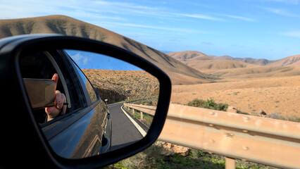 Woman taking photo through car window on volcanic mountain road, Fuerteventura, Spain