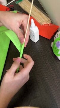 Wrapping a wooden skewer with green floral tape or paper. Making a flower stem. Description: Professional hand movements wrapping a stick with green paper to create a realistic flower stem for a DIY b