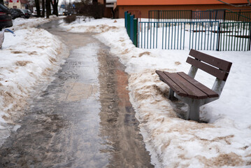 ławeczka przy mokrym chodniku posypanym piachem, w zimowym otoczeniu © Katarzyna