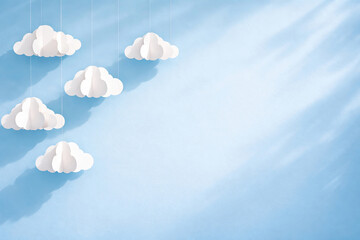 Minimal hanging paper clouds on soft blue background with shadows