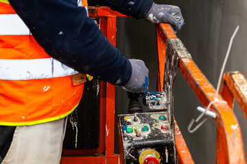 Fototapeta premium Detail of worker’s hand controlling lift machinery during interior wall painting project in commercial industrial building.