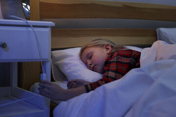 Little girl turning on night lamp before sleep in bedroom