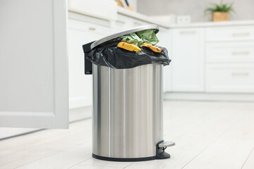 Metal trash bin full of garbage on floor in kitchen © New Africa
