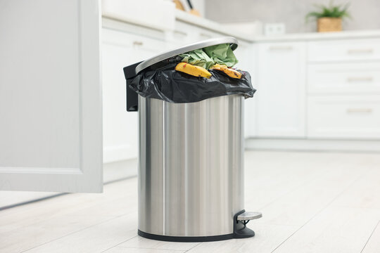 Metal trash bin full of garbage on floor in kitchen