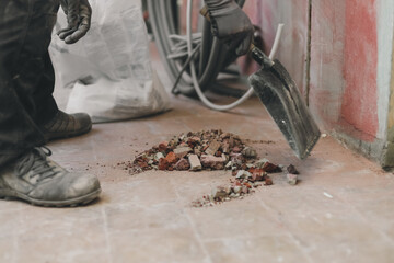 One Caucasian handyman collects construction stones and debris with a scoop.