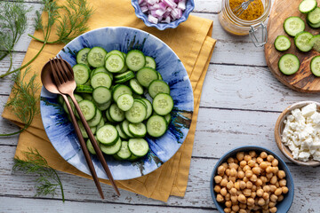 Freshly sliced mini cucumbers with ingredients all around for making a salad.