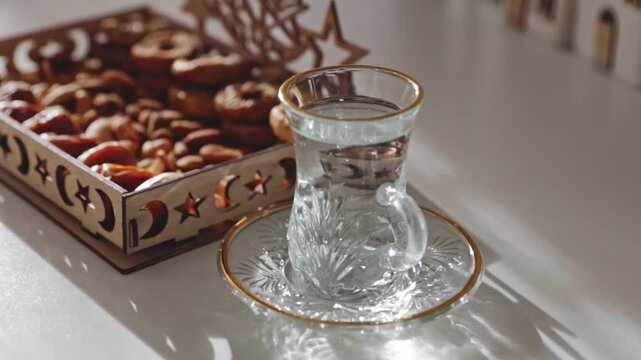 A glass of water and a wooden Ramadan tray with various dried fruits on the table.