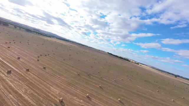 Cinematic aerial 180 degree panorama of hay bales field, descending to ground level with close-up flyby and smooth turn. 4K drone footage