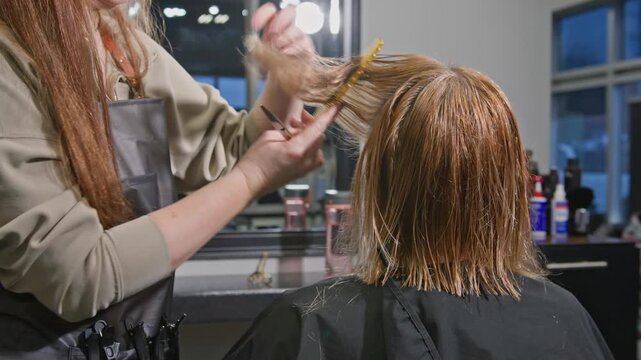 Hairdresser trims split ends and shapes length of woman's hair with scissors while she observes in salon mirror. Relaxed mood, professional tools and perfect preparation for fresh hairstyle in bright