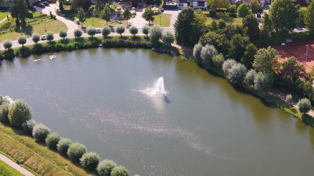 calm oval pond central water fountain tree lined banks sunlit ripples nearby park paths creates quiet residential setting geertruidenberg netherlands tree-lined 