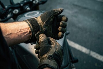 Fototapeta premium A man with veiny arms fastens the strap on his protective motorcycle gloves, preparing for a ride.