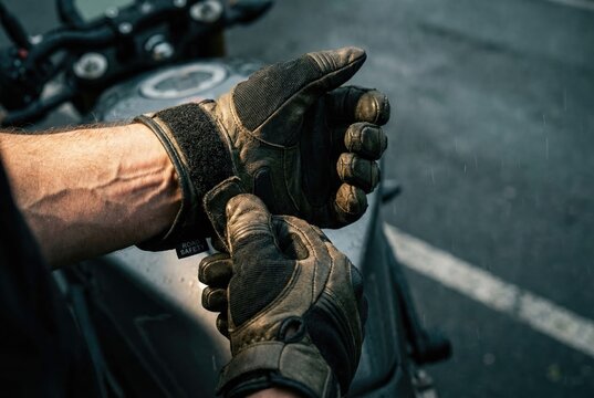 A man with veiny arms fastens the strap on his protective motorcycle gloves, preparing for a ride.