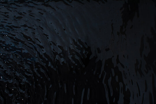 Water with a shining rippled texture on a black background. Abstract black water texture background idea. 