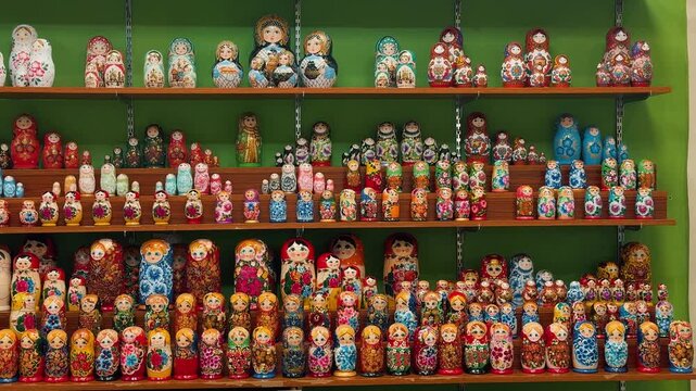 A vibrant display of traditional Russian souvenirs for sale. The camera tilts up showing colorful, hand-painted Matryoshka nesting dolls and ornate music boxes in a market.


