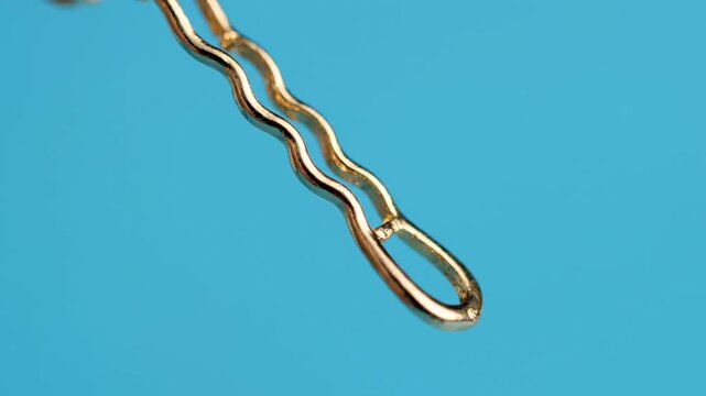 Close-up of a golden bobby pin on a vibrant blue background, showcasing its wavy design and metallic sheen.