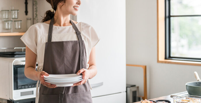 A young Asian woman in an apron doing housework in the kitchen
