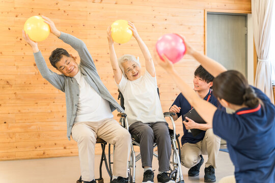 Senior man doing ball exercises at a nursing facility and male and female staff including occupational therapists, physiotherapists and caregivers
