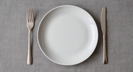 Clean Empty White Dinner Plate with Polished Silver Fork and Knife on Grey Textile, Top View.