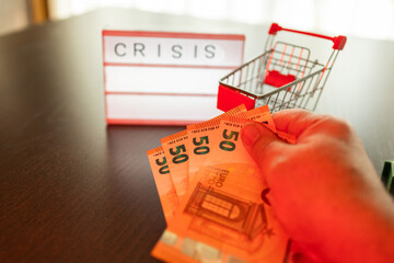 Hand holding euro banknotes with shopping cart and crisis sign