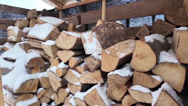 Snow‑covered oak logs stacked in a rustic woodshed during a cold winter day in the countryside.